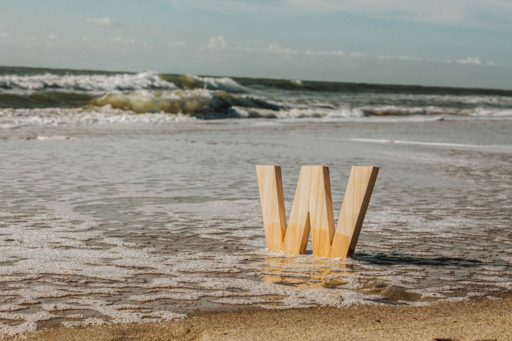 a wooden decoration "w" sitting in the sand with the ocean waves in the background