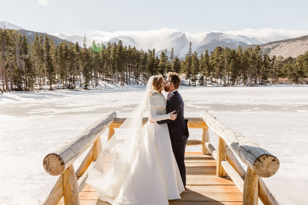 a couple standing at sprague lake kissing during their colorado winter wedding