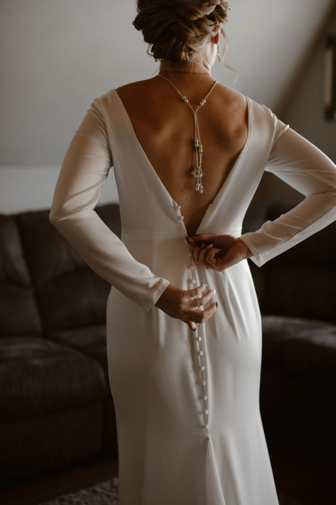 a white women zipping up her long sleeve white wedding dress