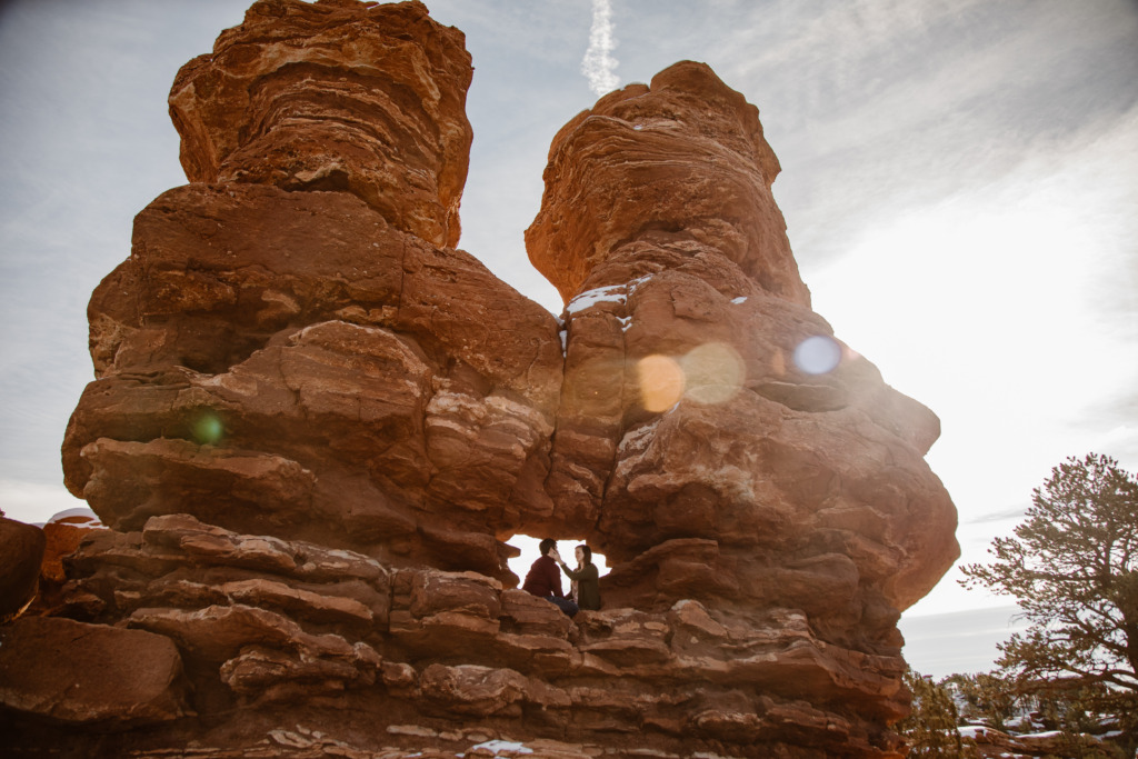 a couple is sitting in the window at the siamese twin sandstone rock formations at garden of the gods with a lens flare 