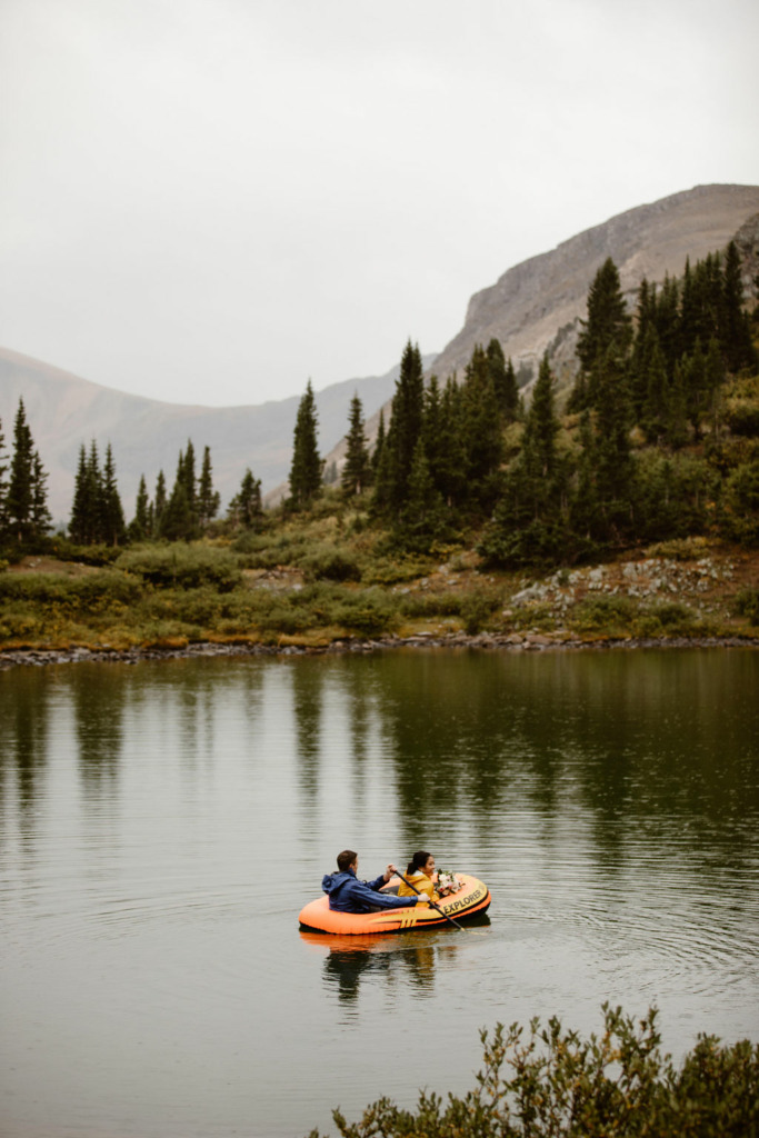 a couple wearing yellow and blue rain jackets are paddling around an alpine lake in colorado on their elopement day