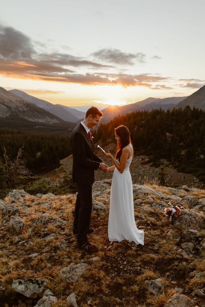 a couple standing on top of a mountain during sunrise wearing wedding attire during their elopement ceremony