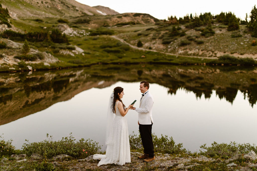 a couple wearing wedding attire holding their elopement next to an alpine lake