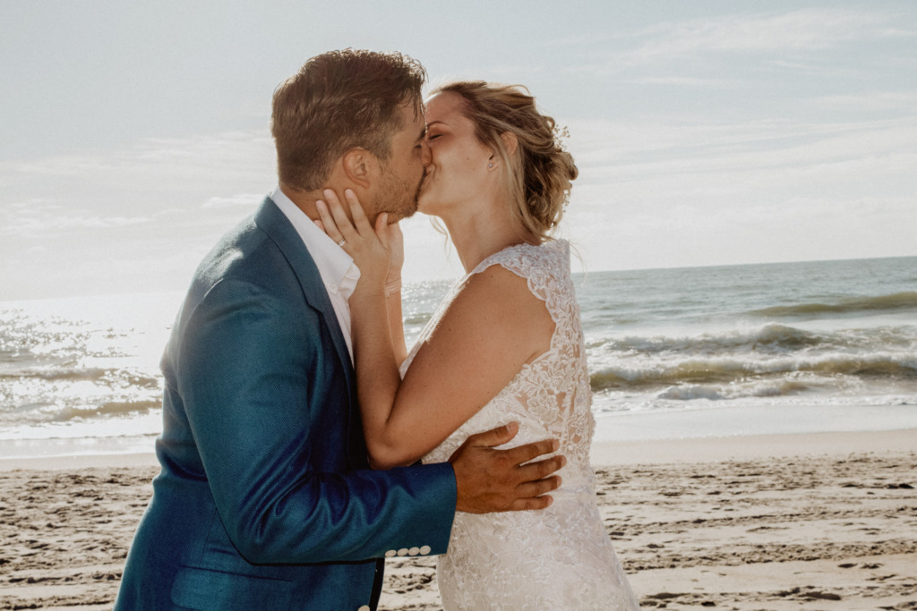 a bride and grooms first kiss next to the ocean during sunrise