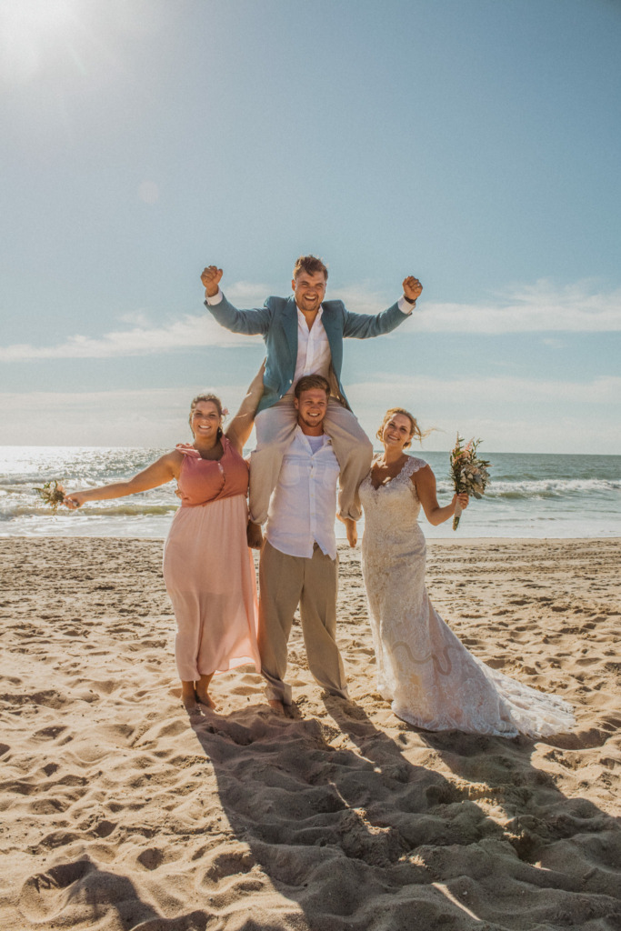 a wedding party poses for a photo on the sandy beach next to the ocean in the morning