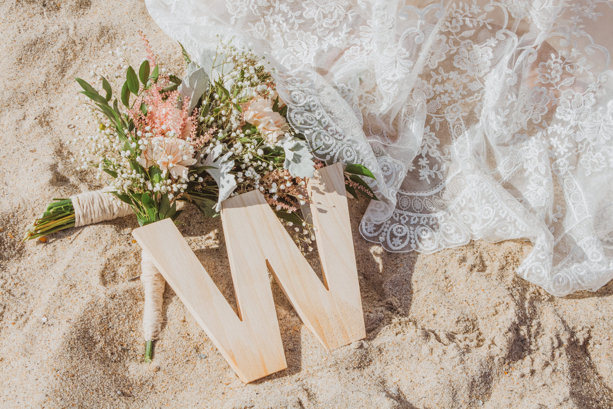 a wooden "w" decoration next to a pink bouquet in the sand