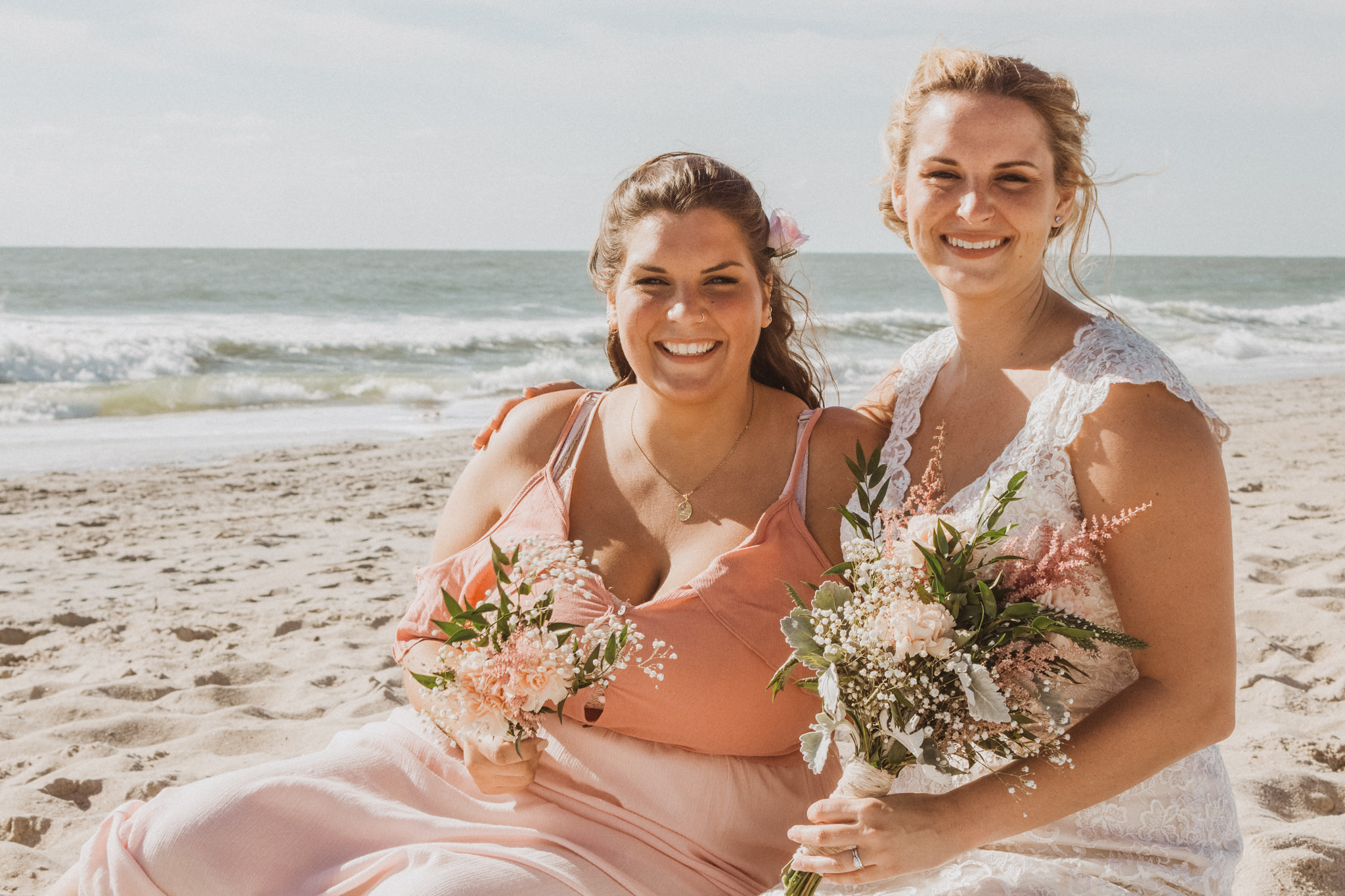a bride and her maid of honor sitting in the sand on a beach