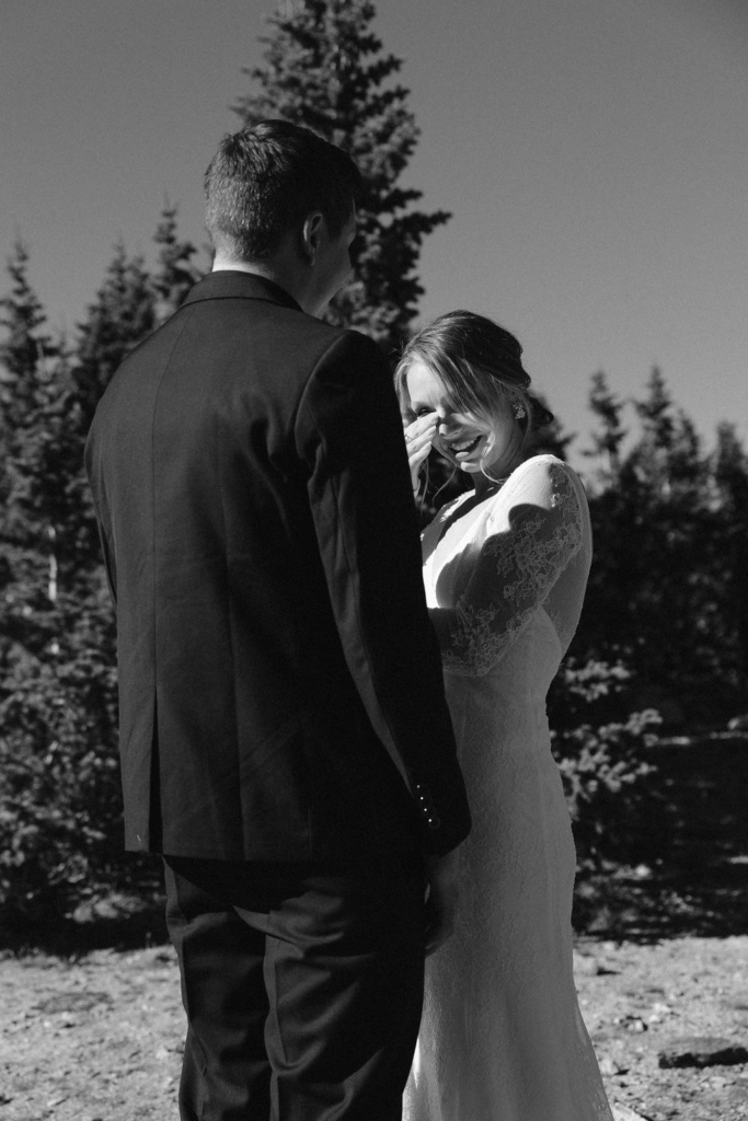 a bride and groom laughing while the bride is wiping a tear off of her face with a big mountain backdrop