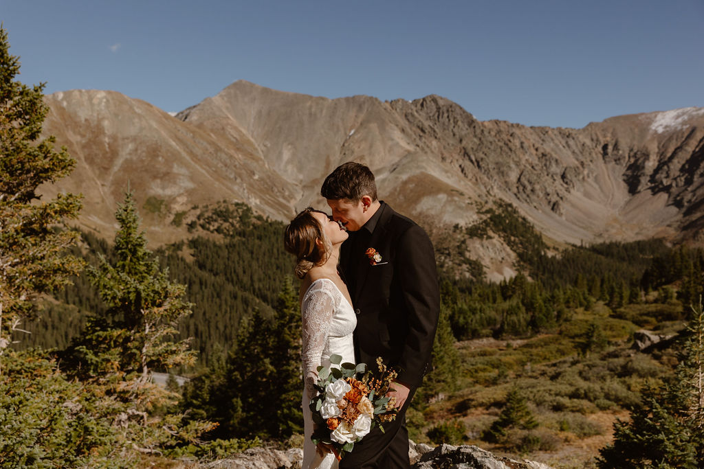 a couple wearing wedding attire kissing with a big mountian backdrop during their loveland pass elopement