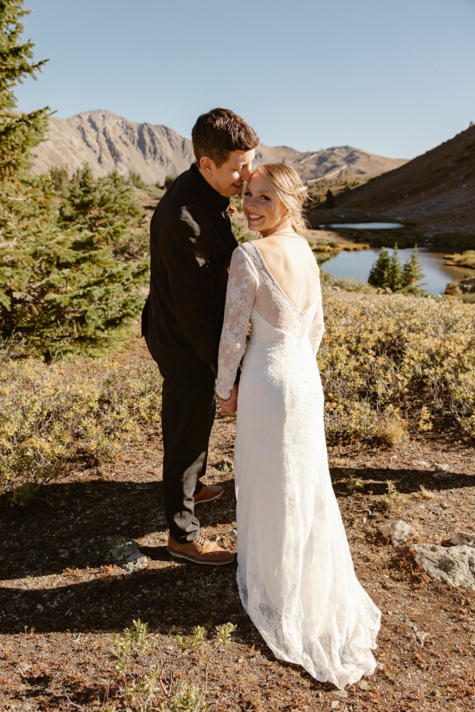 a couple wearing wedding attire standing at the edge of a lake during their loveland pass elopement
