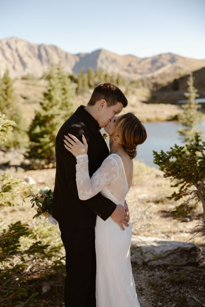 a couple wearing wedding attire standing at the edge of a lake during their loveland pass elopement