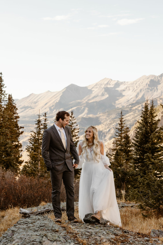 a couple wearing wedding attire holding hands walking towards the camera outdoors during their telluride hiking elopement