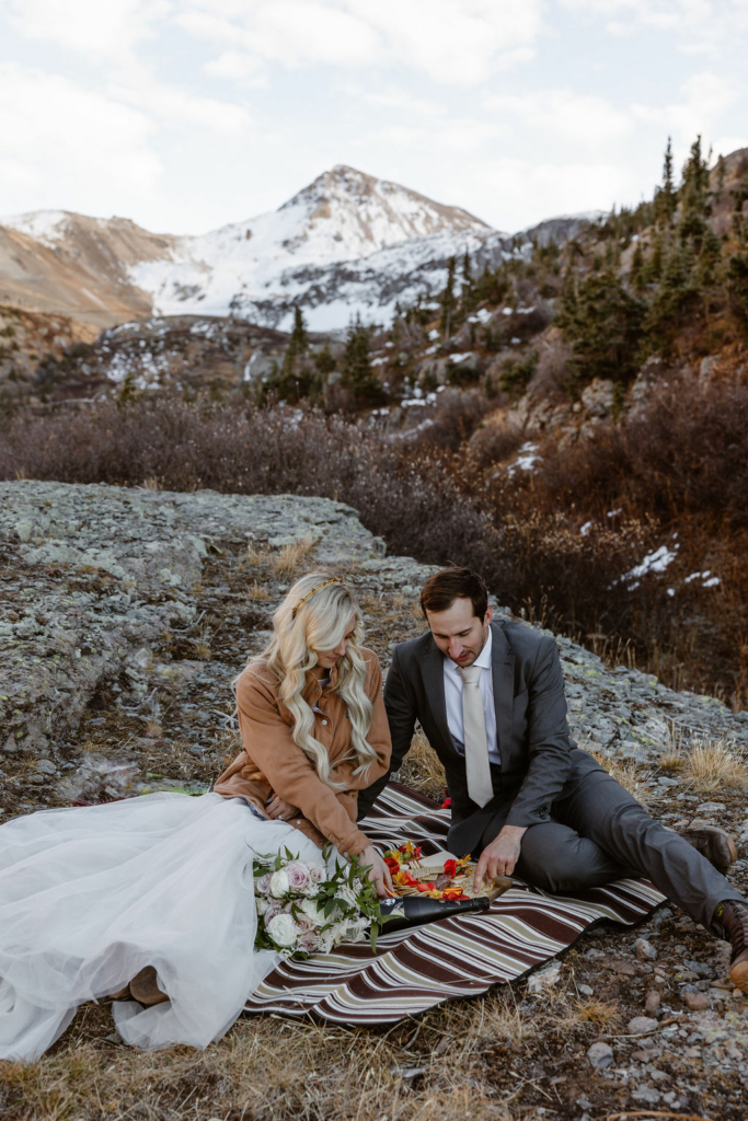a couple sitting outdoors with a picnic blanket and picnic with big mountain backdrop