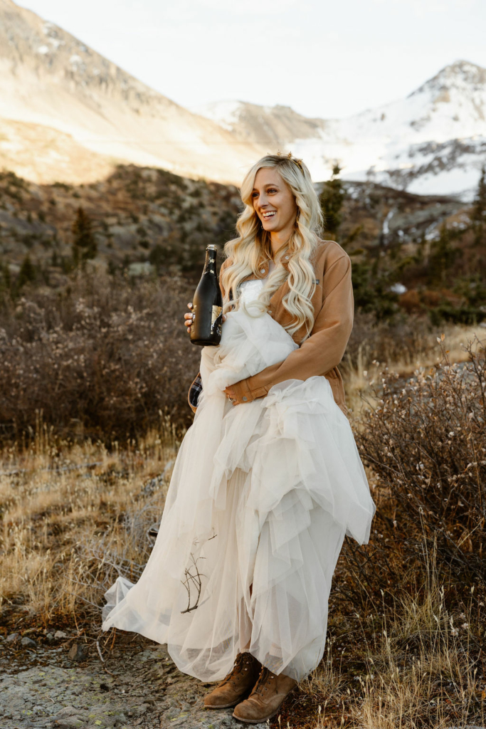 a blonde bride drinking a bottle of champagne outdoors during her telluride hiking elopement
