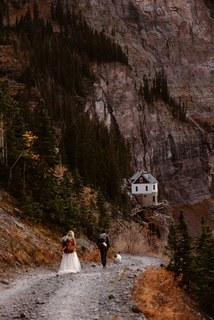 a couple wearing wedding clothes and hiking boots are hiking down a mountain pass in telluride colorado