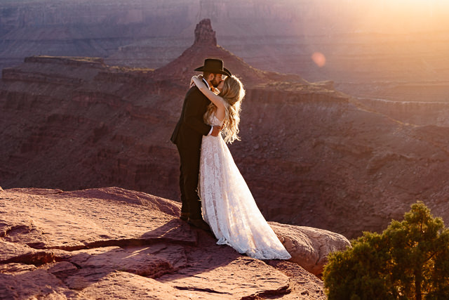 a couple wearing traditional wedding attire kissing at the west bench site ceremony locations during their dead horse point wedding