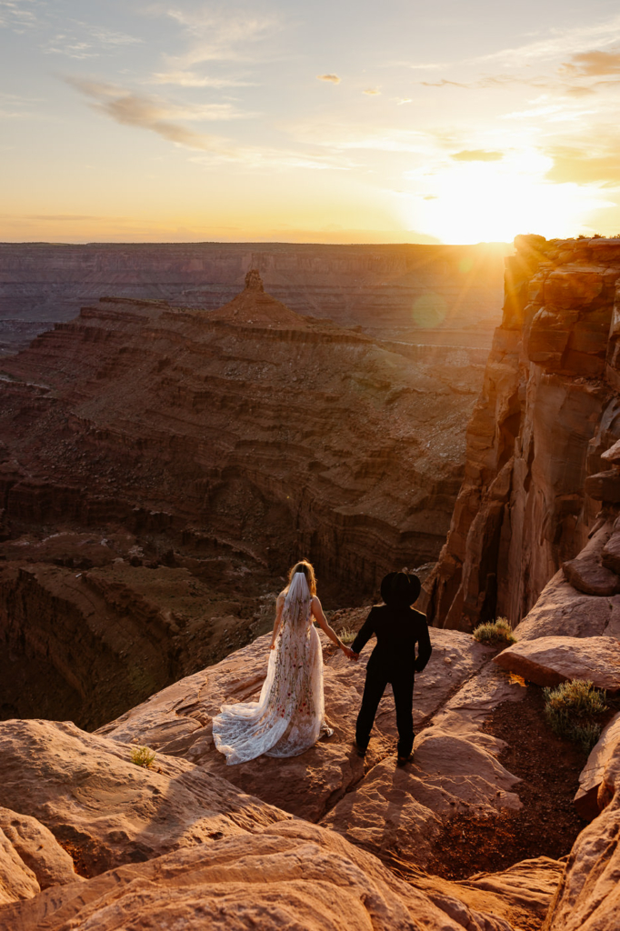 a couple wearing wedding attire holding hands in dead horse point during sunset for their wedding