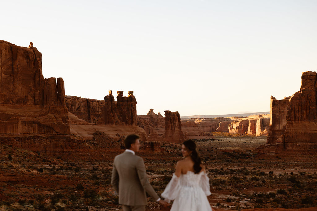 a couple wearing wedding clothes standing at the la sal mountain viewpoint in arches national park 