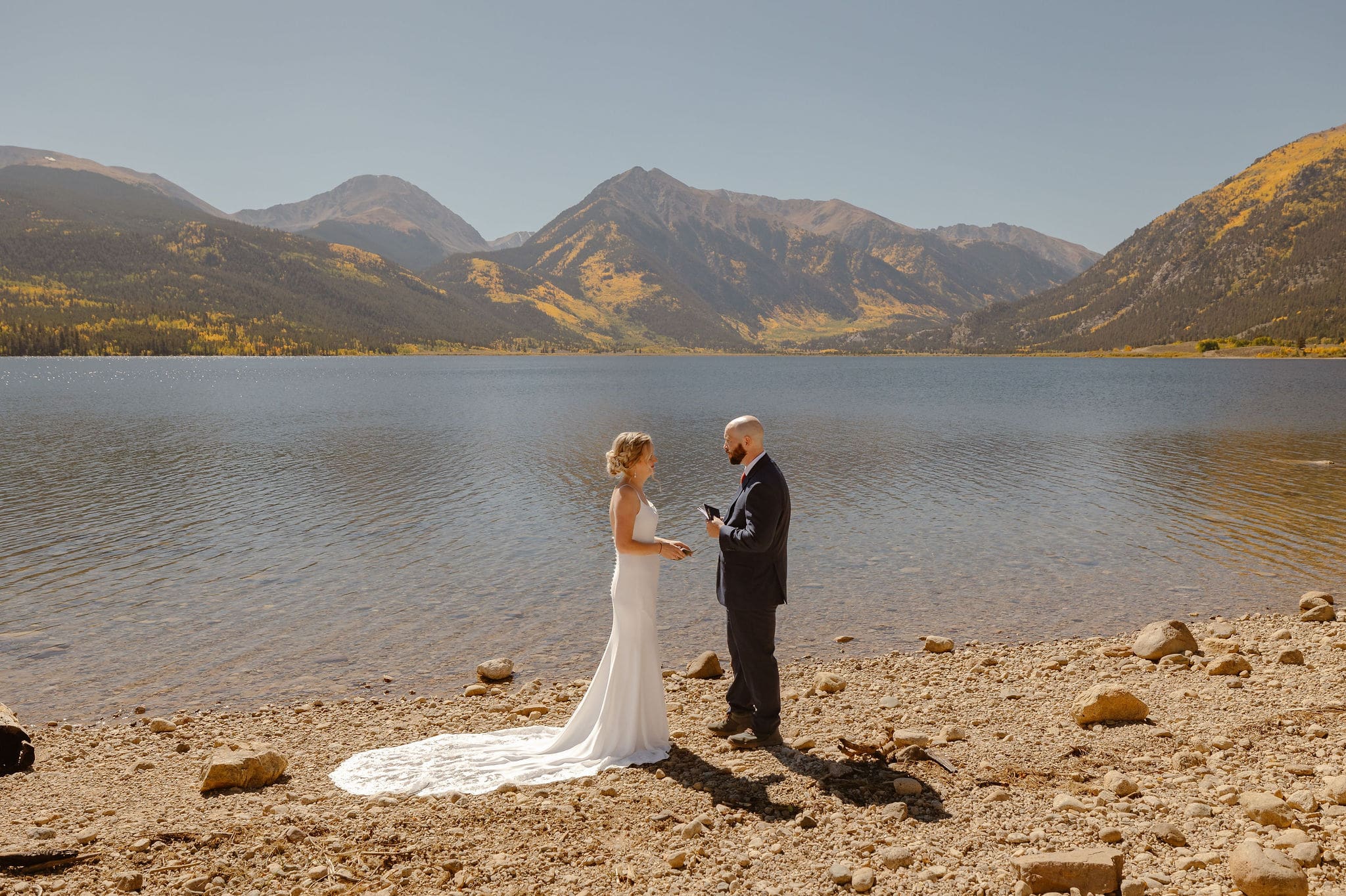 a couple wearing wedding attire standing at the lake shore of twin lakes, colorado