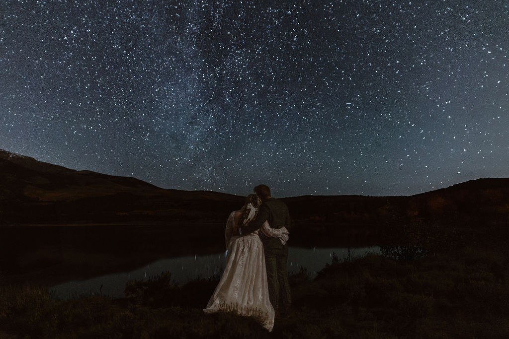 a couple wearing wedding attire is hugging while looking up at the milky way